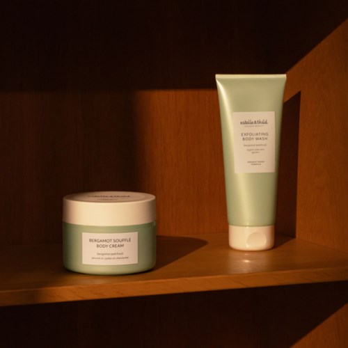 Twee huidverzorgingsproducten, een crème in een pot en een lichaamsvriend in een tube, op een houten plank.