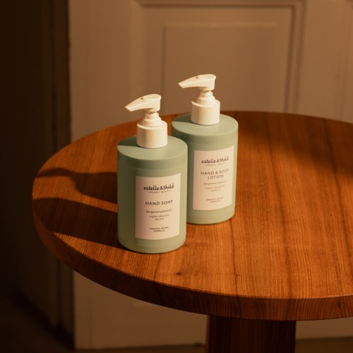 Twee groene flessen handzeep en lotion op een houten tafel, met schaduwen ernaast.