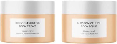 Twee lichaamsverzorgingspotjes met labels voor Blossom Soufflé Body Cream en Blossom Crunch Body Scrub met ingrediënten.