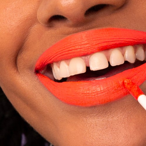 A person is smiling with bright lipstick, showing their white teeth and a small bit of their face.