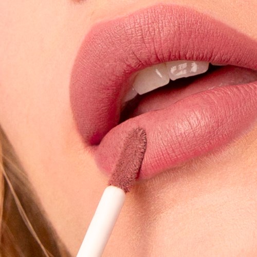 En person som applicerar rosa läppstift eller lip gloss på läpparna med en läppapplikator. Nära bild av mun och sminkverktyg.