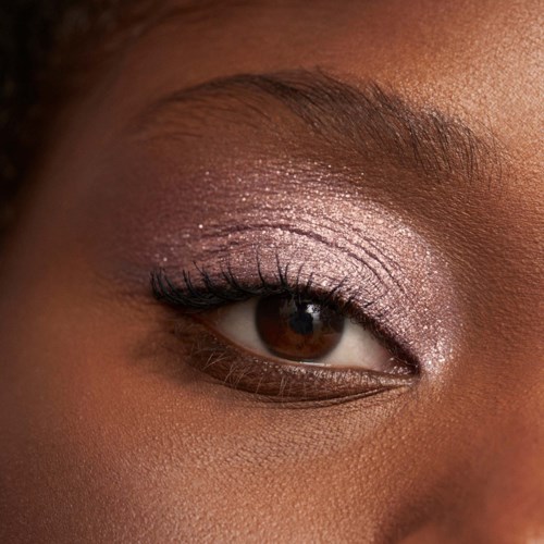 Close-up av ett öga med makeup, brunt hud och välvårdade ögonbryn. Ögat har skimrande ögonskugga och långa ögonfransar.