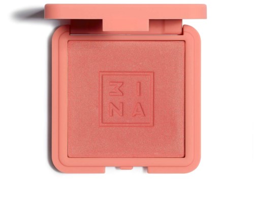 A coral pink blush compact with a square embossed logo inside, open lid casting a shadow.