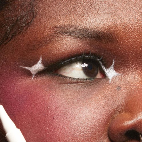 A close-up of a person’s eye with white star-shaped makeup accents around it.