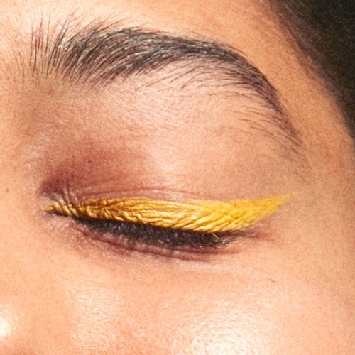 A closed eye with yellow winged eyeliner and natural eyebrows.
