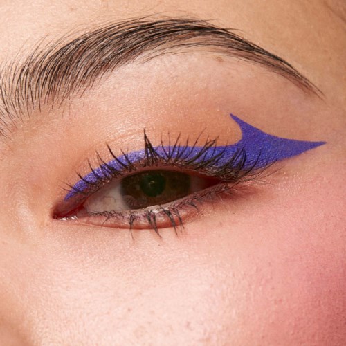 Close-up of an eye with purple eye makeup and a blue arrow painted on the eyelid. Skin is smooth and light-colored.