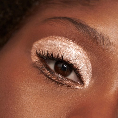 Close-up of a person's eye with shiny, light-colored eye makeup and dark eyelashes.