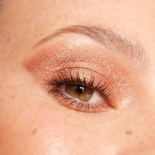 A close-up of an eye with gold eyeshadow, long eyelashes, and a light skin tone.