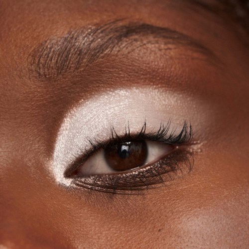 An eye with shiny brown iris, white eyeshadow, and long black eyelashes, surrounded by smooth skin.