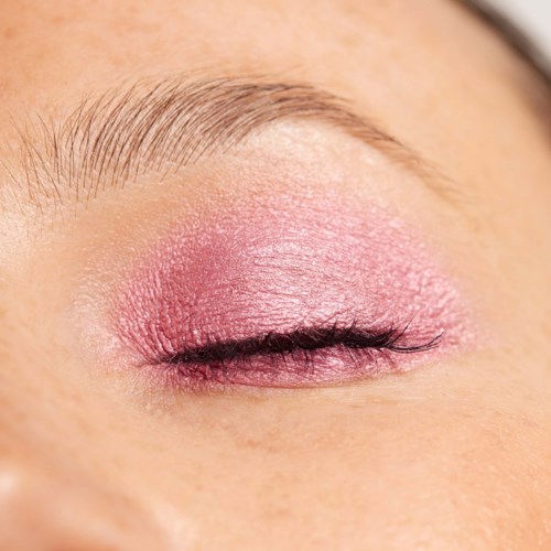 A closed eye with pink eye shadow and natural eyebrow. The eyelashes are visible and well-groomed.