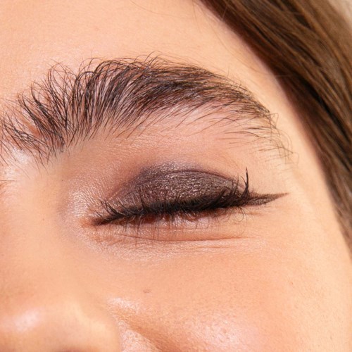 A close-up view of a woman's eye with eyeshadow, eyeliner, and well-groomed eyebrow.