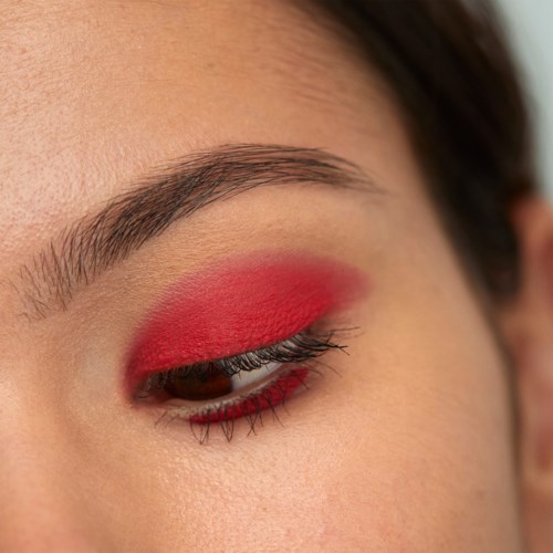 A person has eye makeup with bright red eyeshadow and long eyelashes.
