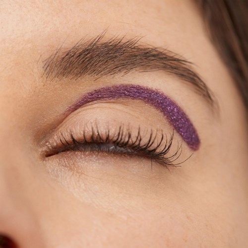 An eye with purple glitter eyeshadow applied in a curved line above the eyelid.