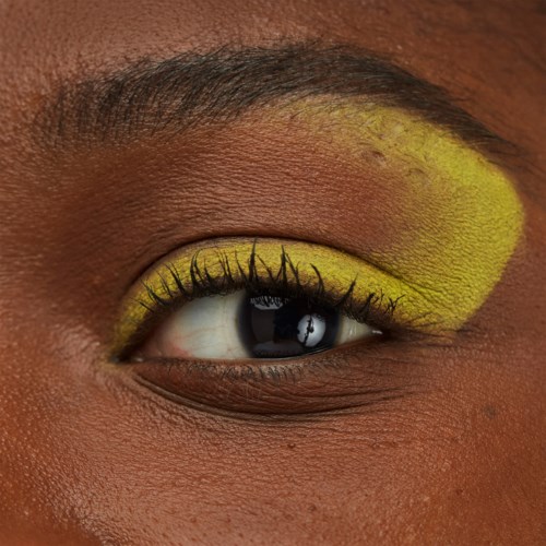 A close-up of a person's eye with bright yellow eyeshadow and long eyelashes.