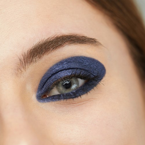 Close-up of an eye with bold blue eye makeup and well-groomed eyebrow.