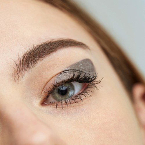 Close-up of an eye with makeup, featuring gray eyeshadow and long eyelashes.