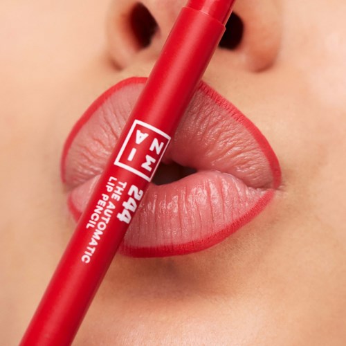 Close-up of lips with red lipstick and a red pencil held between lips. Focus on lips and lipstick.