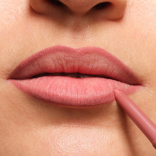 Close-up of lips being colored with a pink lip liner. Skin around lips smooth and well-lit.