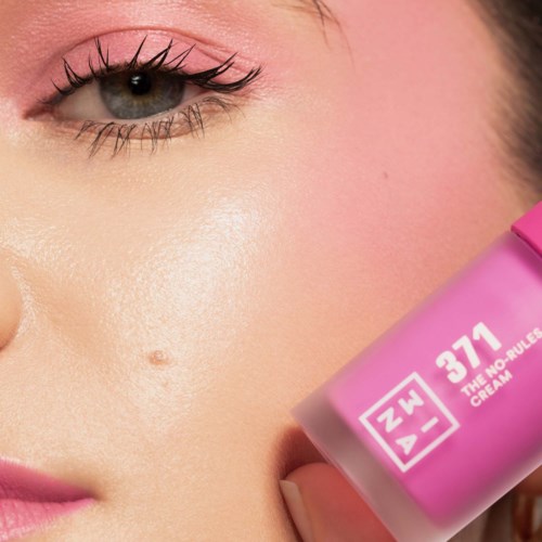 A woman holds a pink bottle labeled '37.1 The No Rules Cream' close to her face.