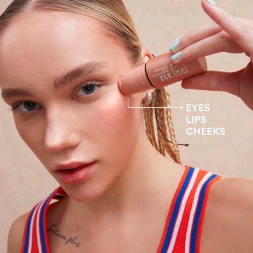 The person is applying makeup near the eye with a tube labeled "Z". The face has clear skin and light hair.