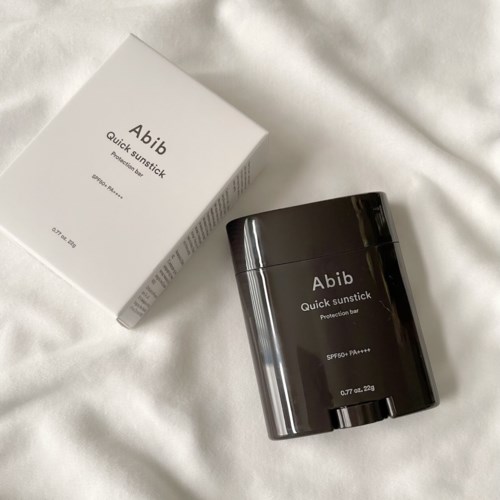Een zwarte compacte container en een witte doos, beide met het label "Abib Quick Sunstick," liggen op een witte ondergrond.