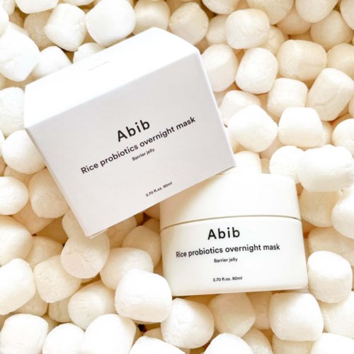 Een witte doos en een pot met 'Abib Rice Probiotics Overnight Mask' erop, omgeven door kleine witte verpakkingsballen.