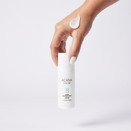 Een hand met witte nagellak houdt een witte fles met het label ACASIA SKINCARE, met crème op de vinger.