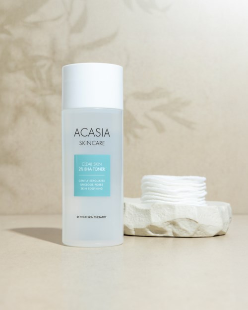 Een witte fles met 'ACASIA SKINCARE' en een blauwe label naast een kleine stapel witte wattenschijfjes.