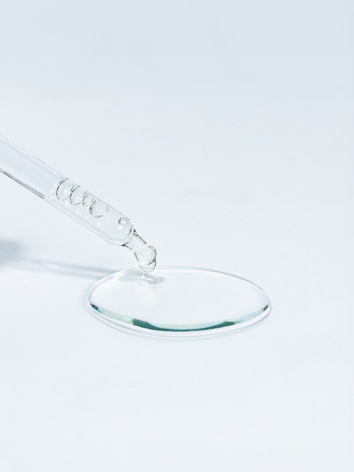 Een pipet geeft vloeistof af op een petrischaal. De scène is schoon, minimalistisch en laboratorium-gerelateerd.