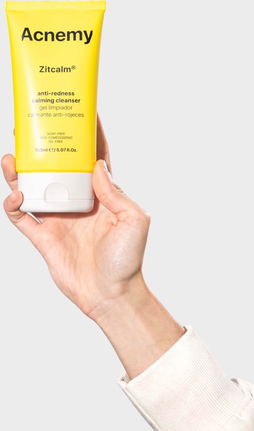 Een hand houdt een gele tube met 'Acne My' label en tekst over kalmering en roodheid. Duidelijke achtergrond.