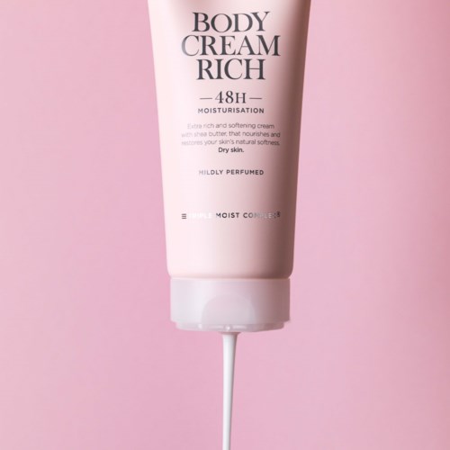 A pink tube of body cream with white text, showing it is rich, moisturizing, and mildly perfumed.