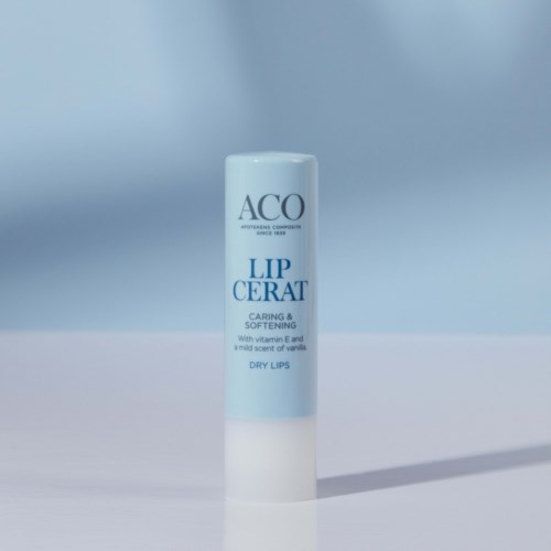 En vit cylinderformad tub märkt 'ACO Lip Cerat' med blå text, står på en ljus yta, kastar skugga.