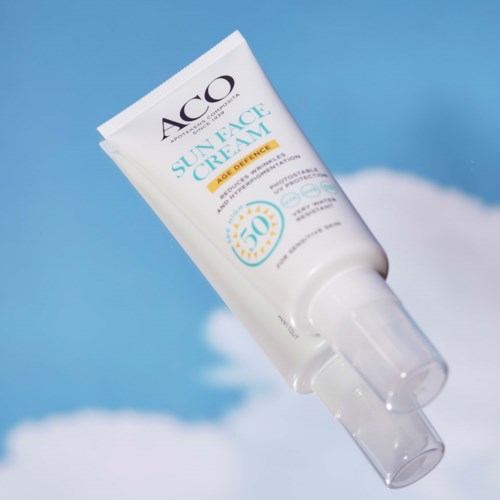 A white tube of sunscreen cream with SPF 50, tilted against a blue sky and clouds background.