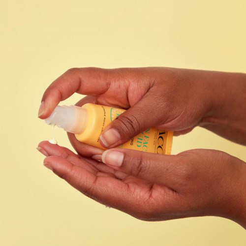En person som applicerar lotion eller kräm från en liten gul flaska på handen.