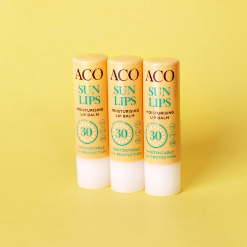 Tre tuber med ACO Sun Lips fuktgivande läppbalsam med SPF 30 står mot en gul bakgrund.