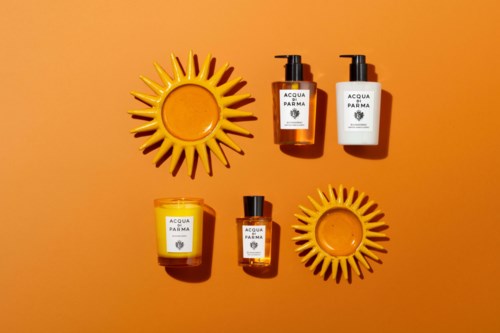 Ihonhoitotuotteet aseteltuna oranssille taustalle auringon muotoisten koristelautasten kanssa, merkilt  Identt ; Acqua di Parma. Yksinkertaista ja kirkasta.