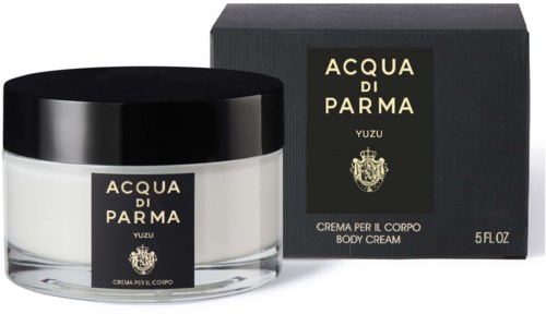 A white body cream in a glass jar with a black lid, next to a black box with gold and white text.
