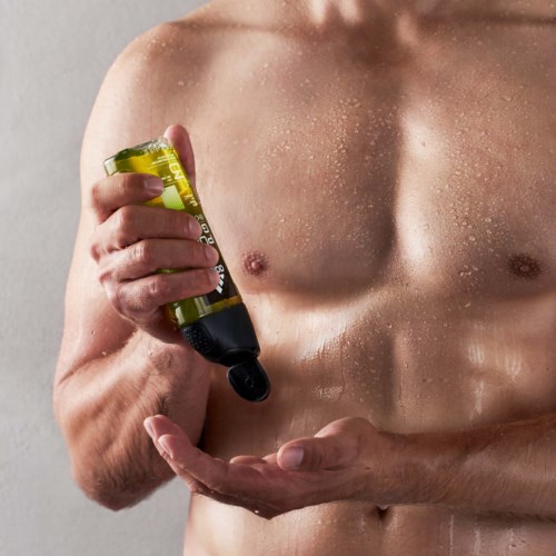 Een naakte man brengt lichaamsolie of lotion aan op zijn borst voor een lichte achtergrond.