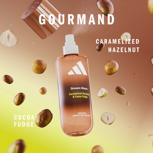 Een spray met caramelized hazelnoot en cocoa fudge smaak, omringd door verspreide hazelnoten en stukjes. Warme kleuren op de achtergrond. GOURMAND tekst bovenaan.