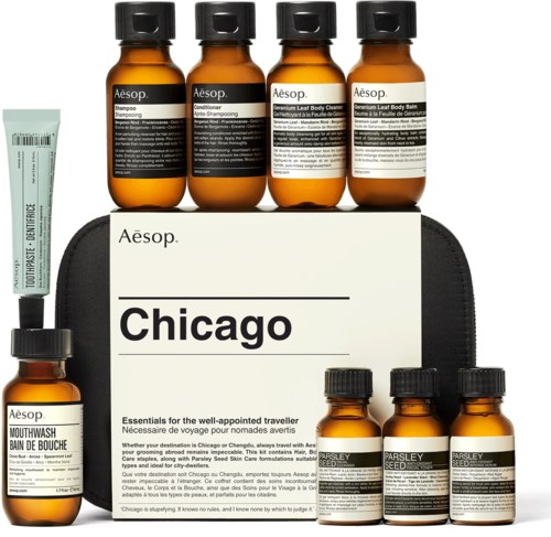 Reisegrößenflaschen mit Aesop-Produkten, einschließlich Shampoo, Conditioner, Körperpeeling, Mundwasser und Nahrungsergänzungsmitteln, auf einer schwarzen Tasche.