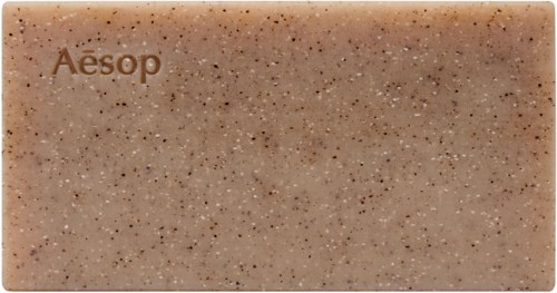 Ein rechteckiges beiges Seifenstück mit kleinen dunkleren Flecken und dem Wort 'Aesop'.