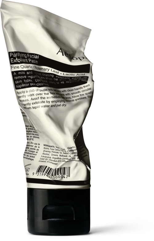 Ein zerknitterter silberner Peeling-Tubus für das Gesicht mit schwarzem Deckel, teilweise mit Text und Barcode.