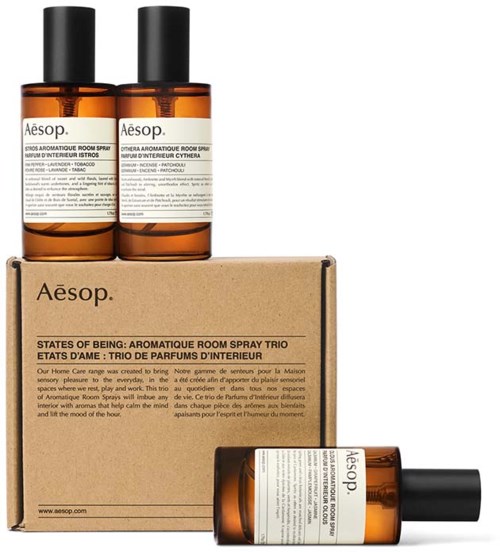 Zwei braune Flaschen von Aesop Aromatic Room Spray, eine liegend, mit einem Karton mit Aesop-Label und Produktdetails.