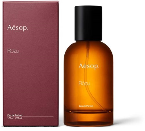 Ein Parfümflasche mit schwarzem Deckel neben einer rosa Schachtel. Die Flasche ist bernsteinfarben und mit 'Aesop Rōzu' beschriftet.