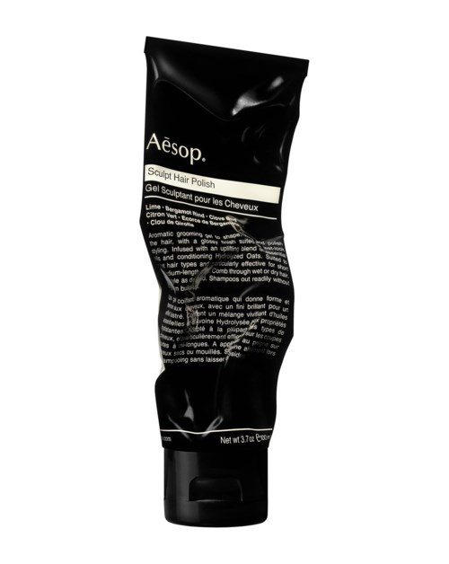 Eine schwarze Tube mit Aesop Kopfhaut-Haarpolish mit weißen und grauen Texten, steht aufrecht.