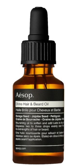 Kleine braune Glasflasche mit schwarzen Tropfenzähler, beschriftet 'Aesop' und 'Shine Hair & Beard Oil'.