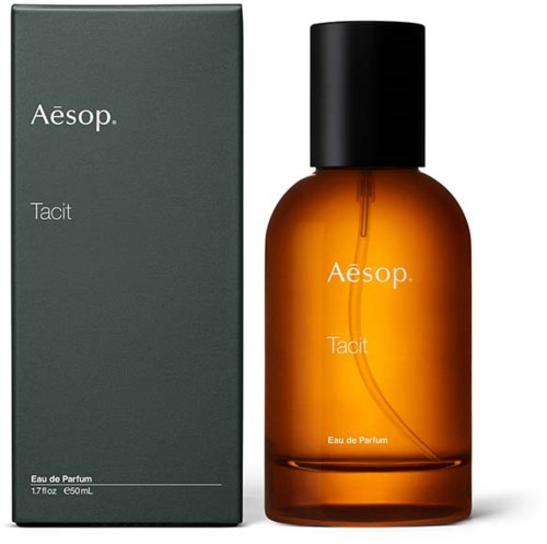 Eine kleine bernsteinfarbene Parfüflasche und eine dunkelgraue Schachtel, beide mit der Beschriftung Aesop Tacit, mit einfachem weißem Text und schwarzem Deckel.