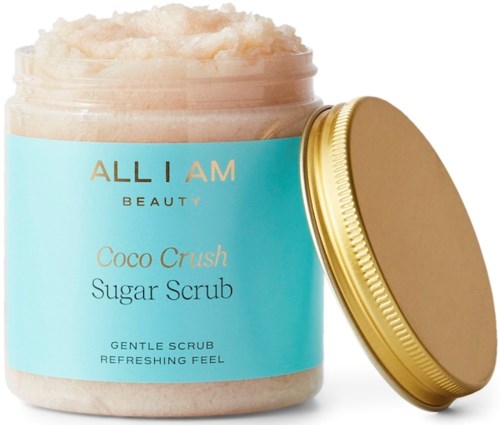 Een blauwe pot met 'Coco Crush Sugar Scrub' erop, gouden deksel, gevuld met een romige, korrelige scrub.