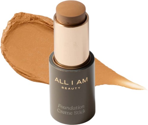 A makeup foundation stick with beige product smeared behind it and the words 'ALL I AM BEAUTY' on the container.