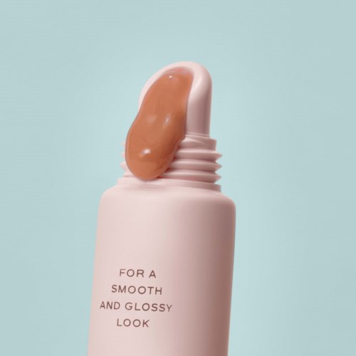 En vit flaska med slogan, med ett beige kosmetikaprodukt som kommer ut. Bakgrunden är ljusblå.